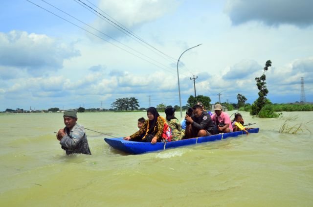 Warga menggunakan perahu melintasi jalan yang tergenang banjir di Karangturi, Setrokalangan, Kudus, Jawa Tengah, Selasa (03/01)