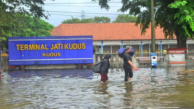 Warga berjalan melintasi Terminal Tipe A Jati yang tergenang banjir di Kudus, Jawa Tengah, Minggu (01/01).